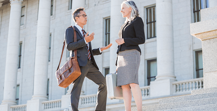 A guy wearing glasses is chatting with a woman in front of a large tall building