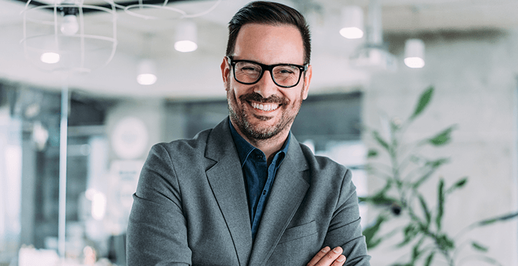 A guy with glasses is crossing his arms and smiling